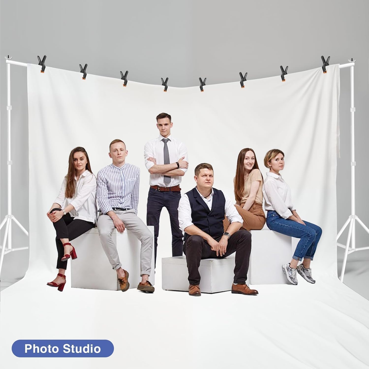 Six adults posing in front of a white fabric backdrop secured with black clamps to a white stand.